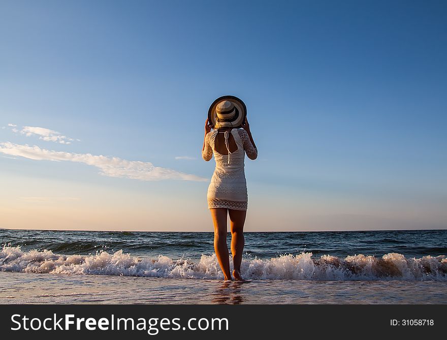 Young woman standing in sea holding her hat and looking ahead. Young woman standing in sea holding her hat and looking ahead