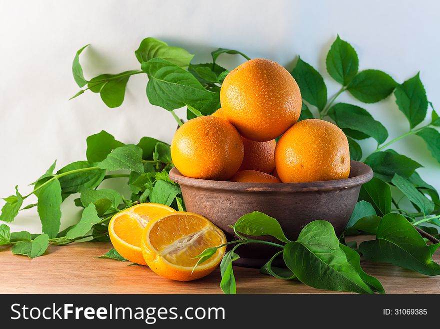 Still life of oranges in a clay bowl with green branches