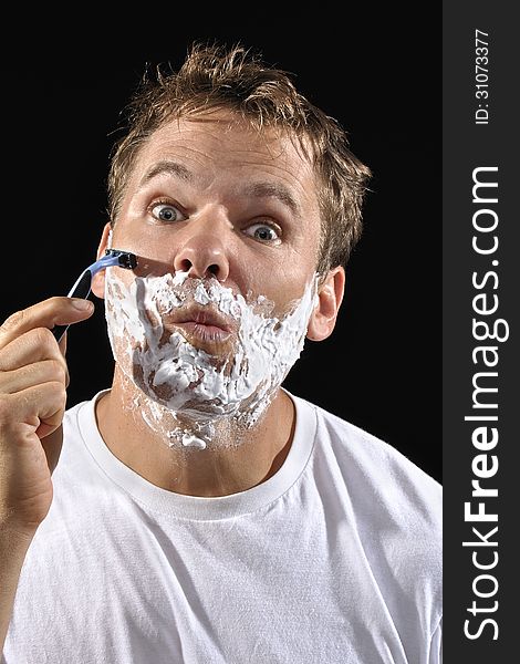 Handsome Caucasian man with messy bed head hair makes funny face while shaving his cheek on black background. Handsome Caucasian man with messy bed head hair makes funny face while shaving his cheek on black background