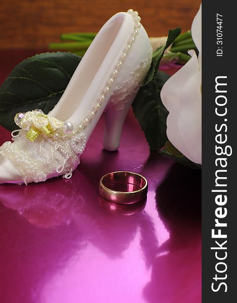 Wedding bridal bouquet of white roses on pink background with good luck shoe and wedding ring. Vertical with copy space.