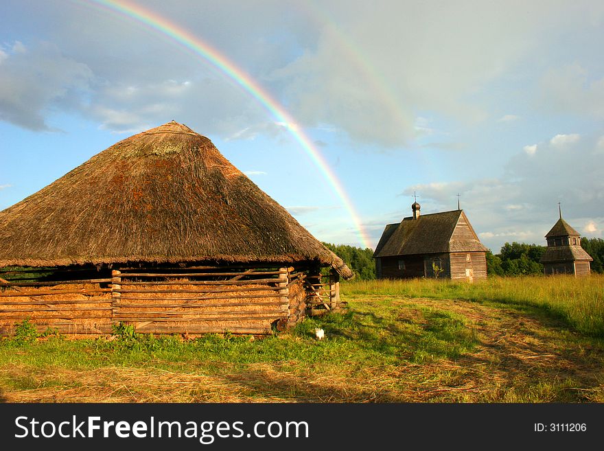 Old wooden small buildings on a background of a rainbow and the dark blue sky. Old wooden small buildings on a background of a rainbow and the dark blue sky
