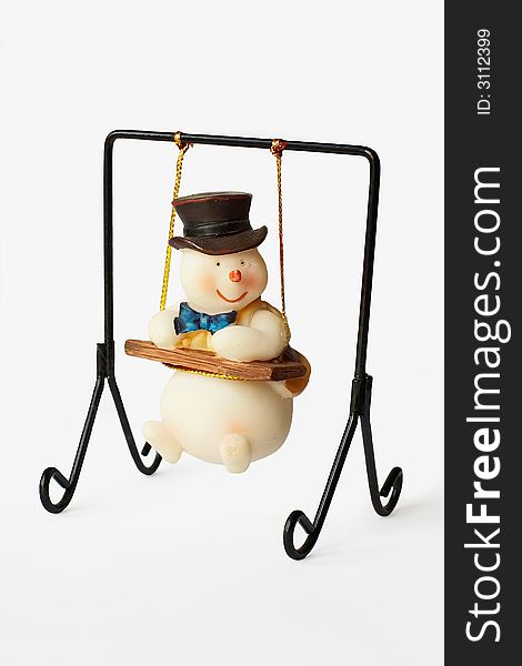 A toy snowman sitting on the swing.He is wearing a high hat.