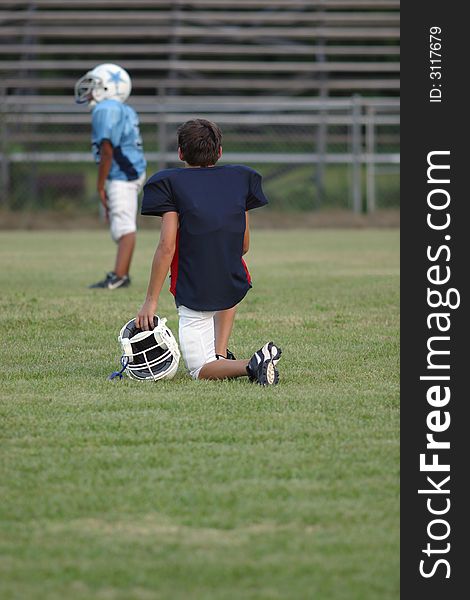 A young boy playing football watches from the sidelines at a game. All logo's and trade names removed from image. A young boy playing football watches from the sidelines at a game. All logo's and trade names removed from image.