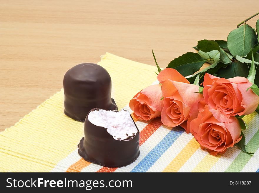 Chocolate candy and roses on yellow tablecloth.