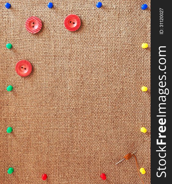 Burlap background decorated with variegated pins, buttons and needle. Burlap background decorated with variegated pins, buttons and needle