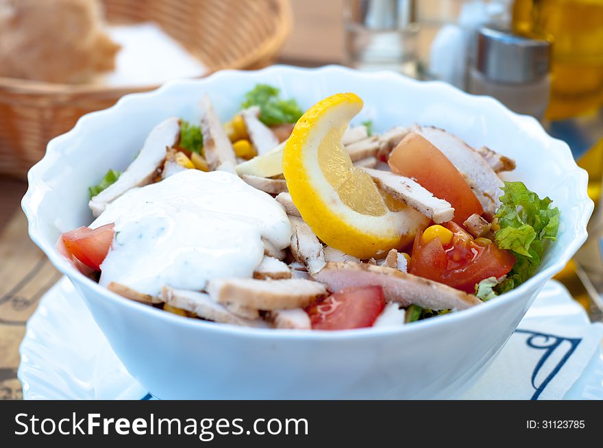 A bow of fresh chicken salad with vegetables and sauce on a table.