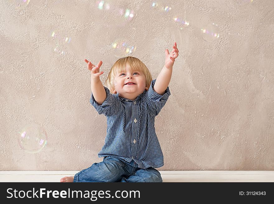 Cute little boy stretching up his arms to catch soap bubbles. Cute little boy stretching up his arms to catch soap bubbles