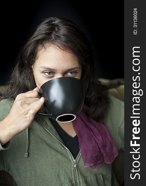 Portrait of a beautiful young woman with striking green eyes drinking coffee from a black cup. Portrait of a beautiful young woman with striking green eyes drinking coffee from a black cup.