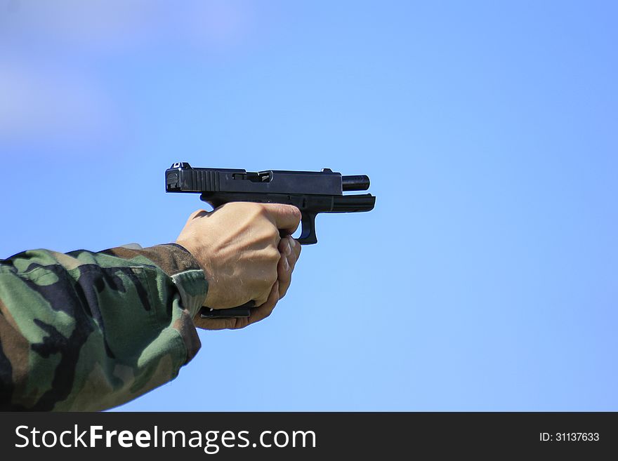 Hands of person shooting Glock 17 with slide back and empty magazine; blue sky background. Hands of person shooting Glock 17 with slide back and empty magazine; blue sky background.