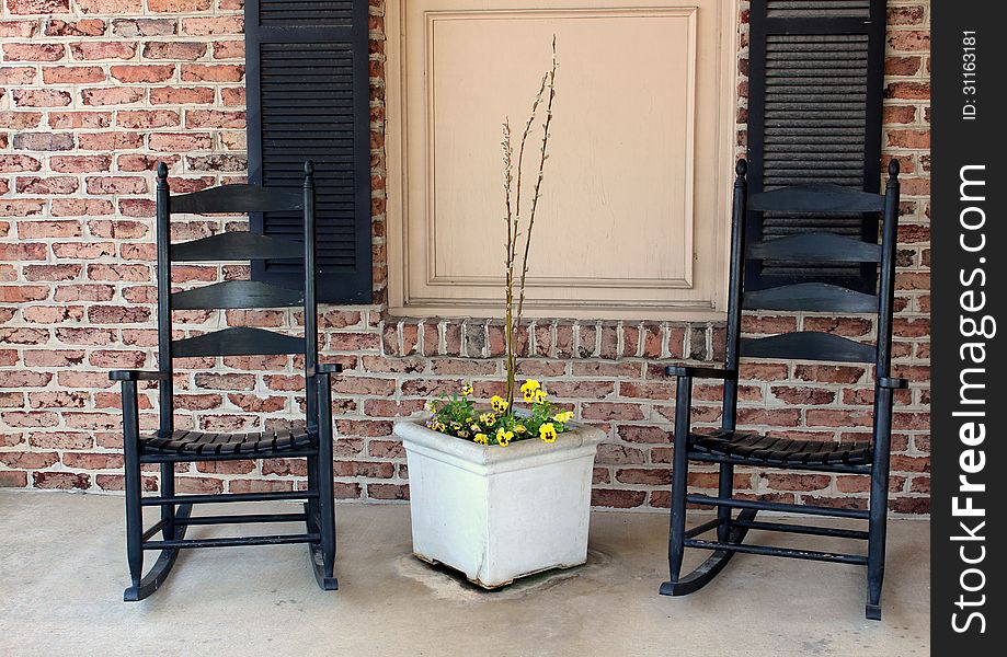 Two black rocking chairs set on a quiet brick porch,inviting people to sit for awhile and take a break from life's sometimes hectic pace. Two black rocking chairs set on a quiet brick porch,inviting people to sit for awhile and take a break from life's sometimes hectic pace.