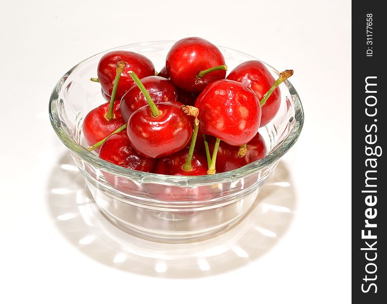 A glass bowl of cherries with a shadow.
