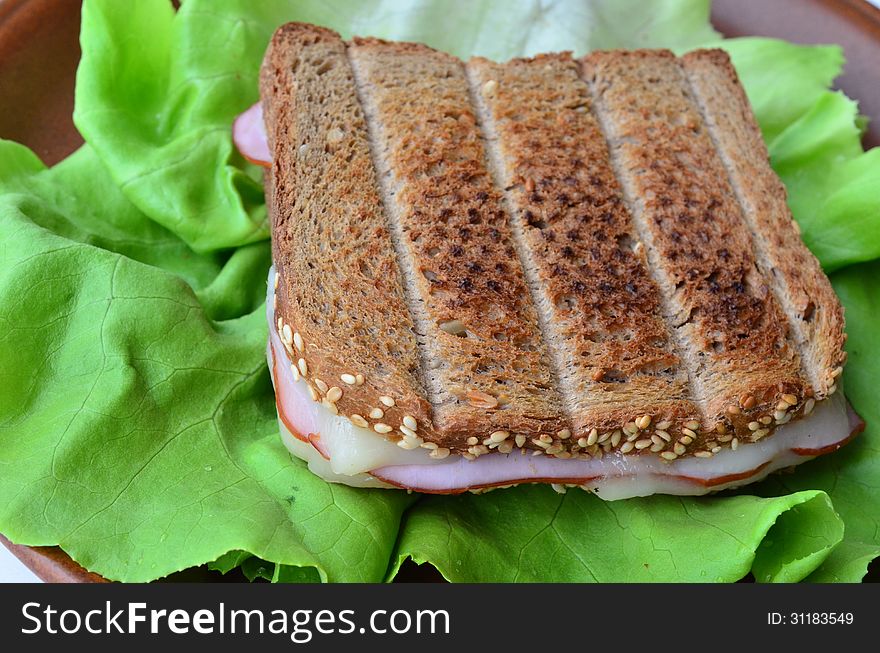 Integral toast with sesame and other whole seeds, ham and cheese sandwich served on a brown porcelain plate over fresh lettuce leaf, a cloaser look. Integral toast with sesame and other whole seeds, ham and cheese sandwich served on a brown porcelain plate over fresh lettuce leaf, a cloaser look