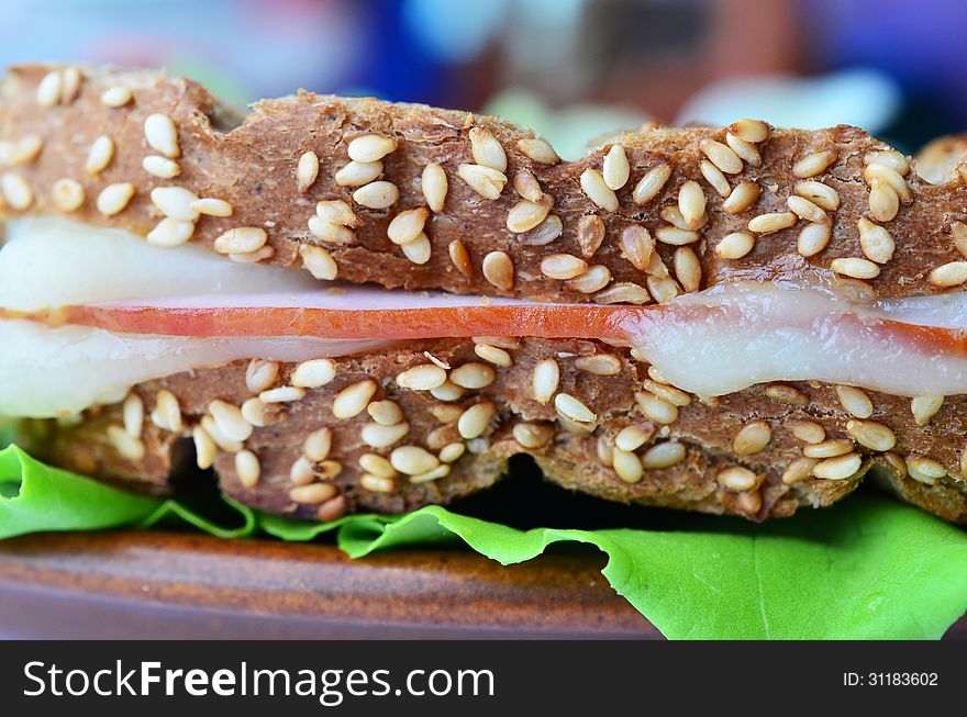 Integral toast with sesame and other whole seeds, ham and cheese sandwich served on a brown porcelain plate over fresh lettuce leaf, close up, side view. Integral toast with sesame and other whole seeds, ham and cheese sandwich served on a brown porcelain plate over fresh lettuce leaf, close up, side view