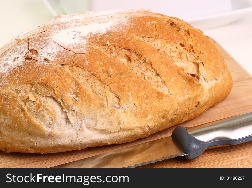 A sideview closeup of a crusty loaf of whole wheat bread on a cutting board ready for serving. A sideview closeup of a crusty loaf of whole wheat bread on a cutting board ready for serving.