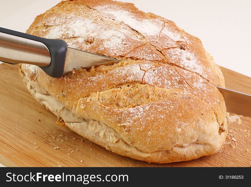 A loaf on a cutting board with a knife cutting into the bread. A loaf on a cutting board with a knife cutting into the bread.