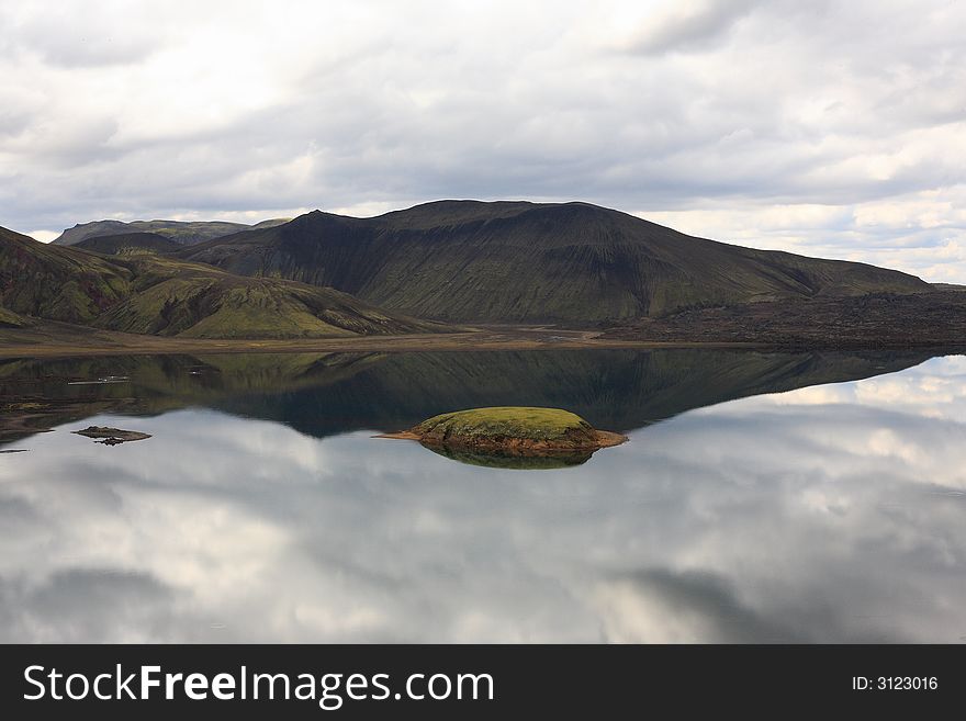 Cloudy sky reflected in the lake inside the  Iceland high hills. Cloudy sky reflected in the lake inside the  Iceland high hills