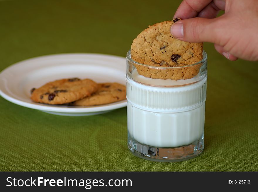 Dipping oatmeal raisin cookies into a glass of milk with a plate of cookies in the background. Dipping oatmeal raisin cookies into a glass of milk with a plate of cookies in the background.