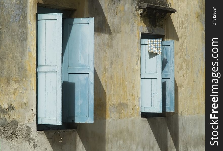 Two windows with open, blue wooden blinds on an old concrete wall. Two windows with open, blue wooden blinds on an old concrete wall