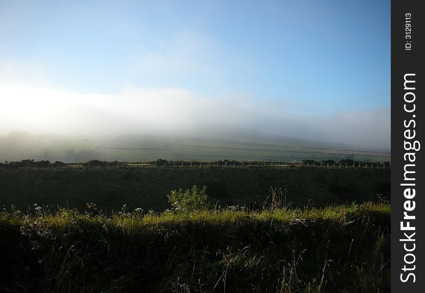 A mist of fog sweeping in over the moor rapidly contrasting against the blue sky. A mist of fog sweeping in over the moor rapidly contrasting against the blue sky