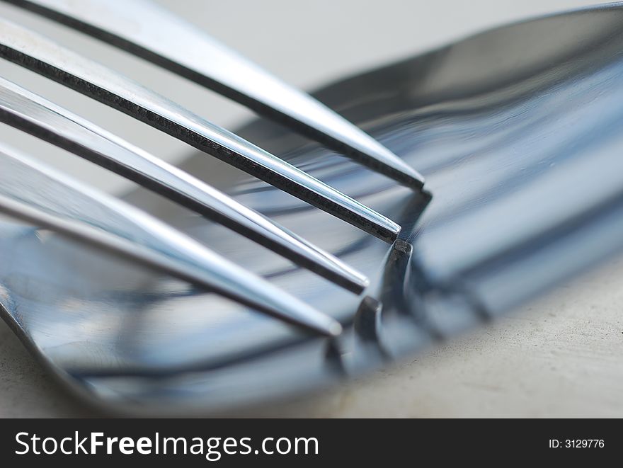 A close-up image of a fork resting in a spoon. A close-up image of a fork resting in a spoon