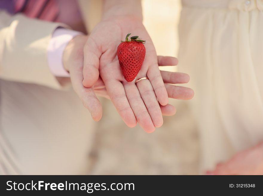 Close-up on hands of bride and groom is ripe strawberries