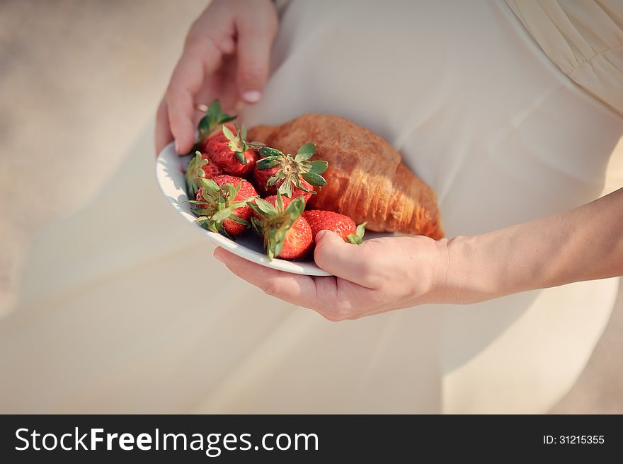 Woman's hands holding a white plate with strawberries and a croissant