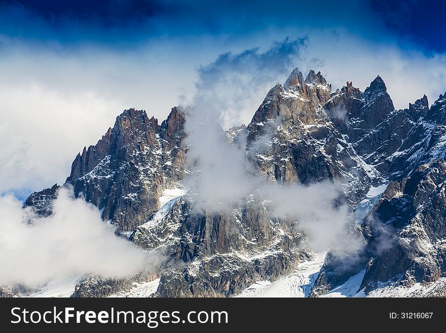 Snow covered mountains, clouds and rocky peaks in the French Alps