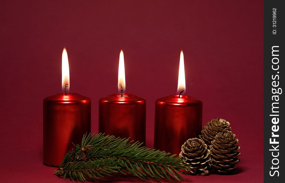Burning red candles with twig of spruce