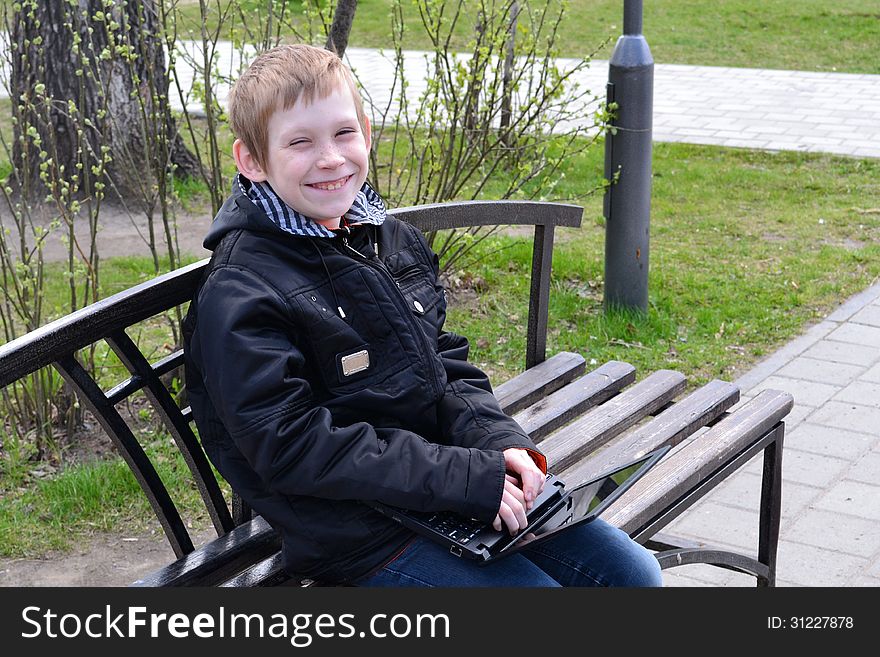 The teenager with the laptop sits on a bench in park