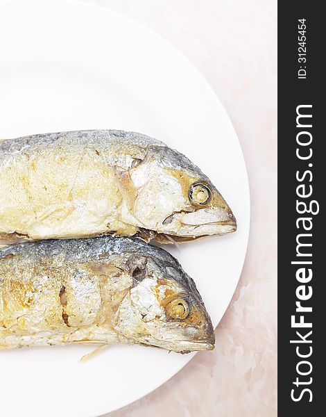 Two fried mackerel fishes on white plate