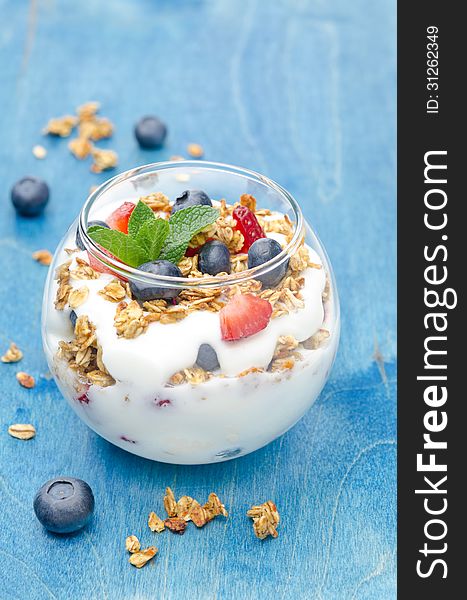 Layered dessert with yogurt, granola, fresh berries in a glass on a blue background