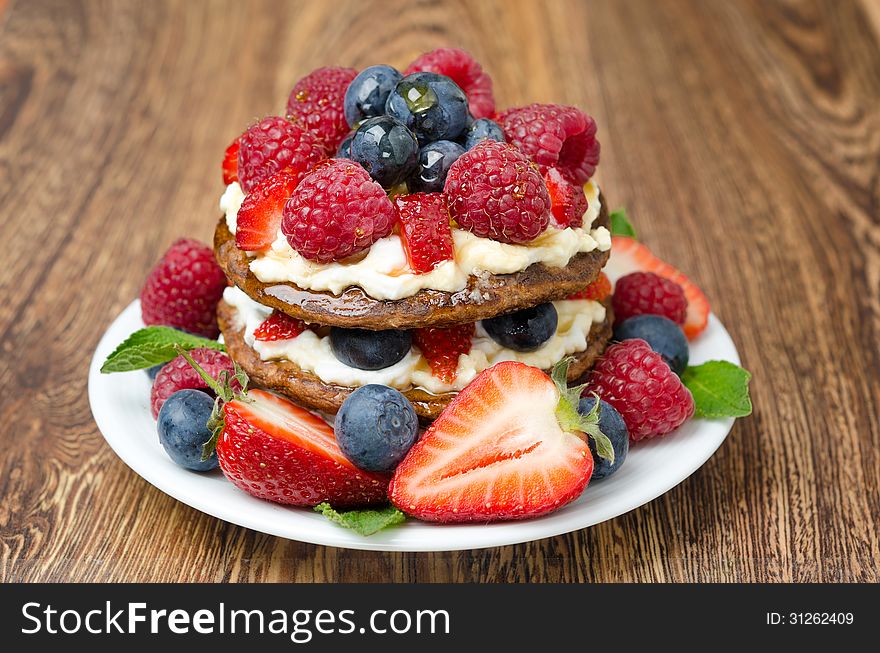 Pancake cake with whipped cream and fresh berries on the wooden table closeup. Pancake cake with whipped cream and fresh berries on the wooden table closeup
