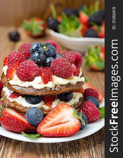 Pancake cake with whipped cream and fresh berries, bowl of berries in the background, close-up vertical