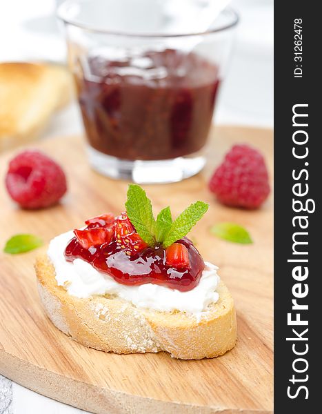 Piece of toasted baguette with cream cheese, raspberry jam and raspberries on a wooden board