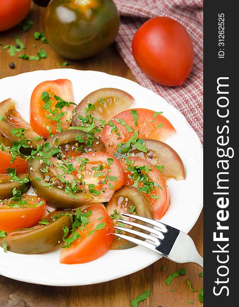 Salad of two varieties of tomatoes with fresh parsley on the plate on a wooden table