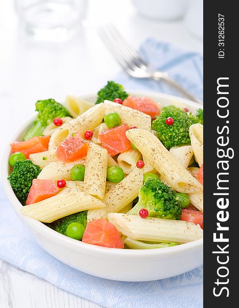 Salad with pasta, smoked salmon, broccoli and green peas in a white bowl close-up. Salad with pasta, smoked salmon, broccoli and green peas in a white bowl close-up