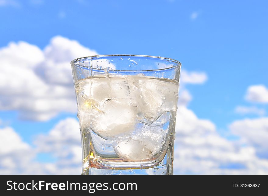 A glass glass of iced water on the background of blue sky. A glass glass of iced water on the background of blue sky