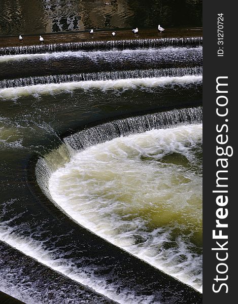 Pulteney Weir in Bristol, England, with white water cascading down a number of steps, and seaguls bathing at the top step. Pulteney Weir in Bristol, England, with white water cascading down a number of steps, and seaguls bathing at the top step