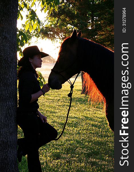 A cowgirl bonds with her horse at sunrise on the farm. A cowgirl bonds with her horse at sunrise on the farm