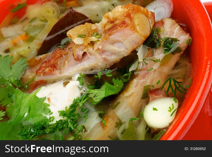 Vegetable Soup with Cabbage, Leek, Carrot, Garlic Greens, Smoked Pork Ribs and Sour Cream closeup in Red Bowl