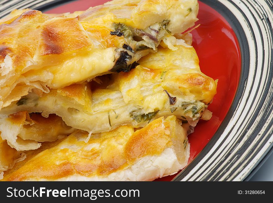 Slices of Cheese and Greens Puff Pastry Pie closeup on Red Plate. Slices of Cheese and Greens Puff Pastry Pie closeup on Red Plate