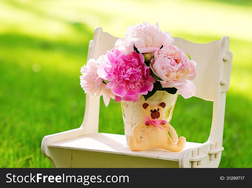 Delicate peonies and teddy bear on a chair on the green lawn. Delicate peonies and teddy bear on a chair on the green lawn