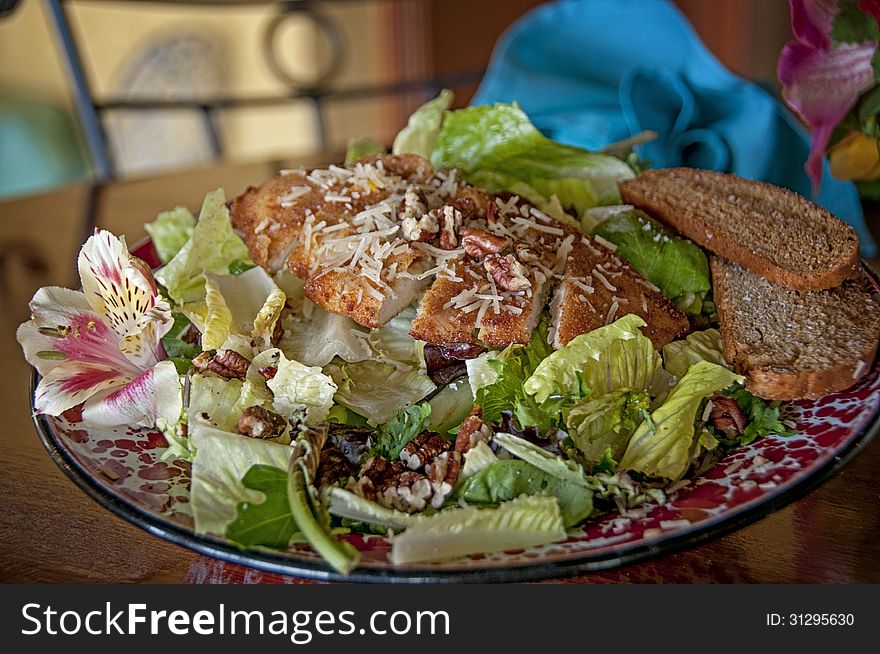 This is a chicken salad with flowers, nuts, and bread. with iceberg lettuce