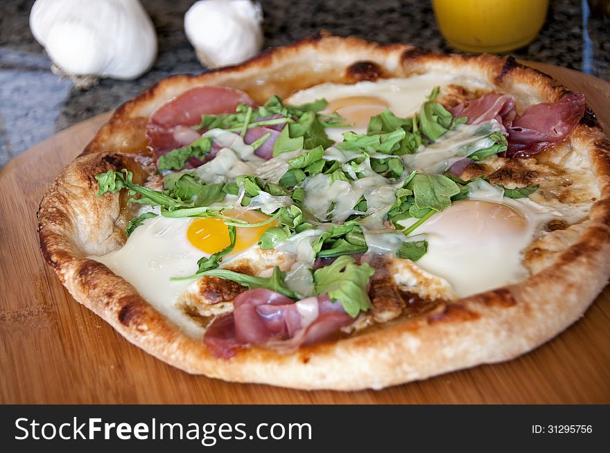 This is a homemade pizza with eggs, ham, and arugula, and cheese