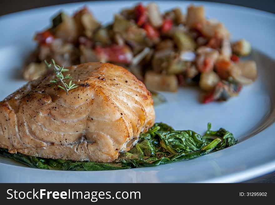This is a baked salmon with a spinach garnish. topped with a rosemary garnish on top. this lots of potatoes as a side