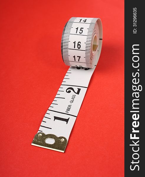 A rolled up white tape measure with both inches and centimetres on a red paper background
