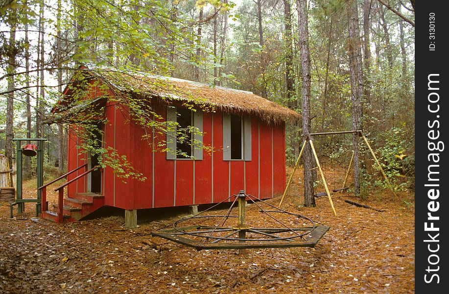 Little Red School House nestled among the trees showing playground equipment in the foreground and a old time school bell in the background