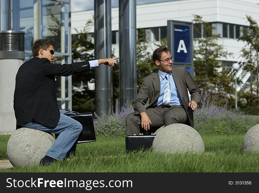 Two young business men sitting outside and pointing on something. Two young business men sitting outside and pointing on something