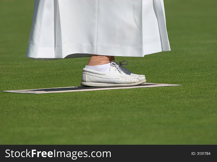 Ankles and feet of an elderly female wearing a long white skirt and white lawn bowling shoes, standing on a mat on a lawned area. Ankles and feet of an elderly female wearing a long white skirt and white lawn bowling shoes, standing on a mat on a lawned area.