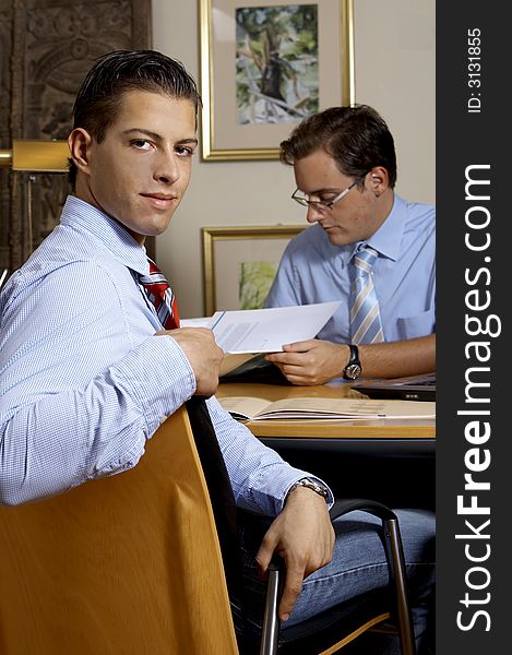 Young business man is smiling while his partner is doing the work. Young business man is smiling while his partner is doing the work